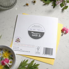 Load image into Gallery viewer, Greetings card with illustration of passion flower. The is the back of the card shoing the barcode and branding. The card is on a table surrounded bu small cut flowers