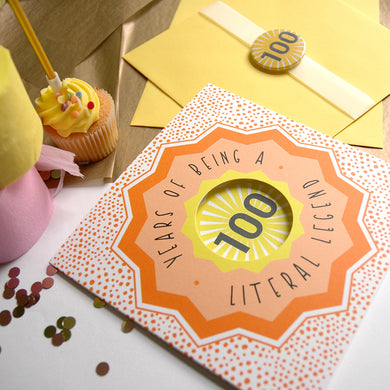 Card with '100 Years of Being a Literal Legend' text on a table with a cupcake and envelope.