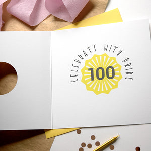 Card with 'Celebrate with Pride 100' design on a wooden surface with decorative elements.