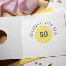 Load image into Gallery viewer, Greeting card with &#39;Celebrate with Pride 50&#39; design on a wooden surface with pink ribbons.