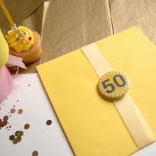 Load image into Gallery viewer, Yellow envelope with a &#39;50&#39; button badge and a cupcake on a wooden surface
