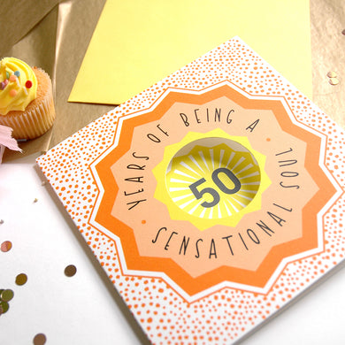 Greeting card with '50 Years of Being a Sensational Soul' text on a wooden surface with a cupcake.