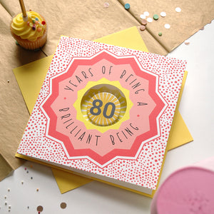 80th birthday card with decorative elements on a table with a cupcake.
