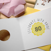 Load image into Gallery viewer, Greeting card with &#39;Celebrate with Pride 80&#39; design on a wooden surface with pink flowers and confetti.