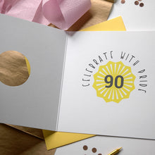 Load image into Gallery viewer, Greeting card with &#39;Celebrate with Pride 90&#39; design on a wooden surface with decorative elements.