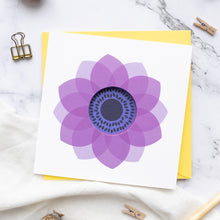 Load image into Gallery viewer, A greeting card with a purple anemone flower design in a circle cut format, accompanied by a yellow envelope, displayed on a marble surface with clips and a pen.