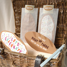 Load image into Gallery viewer, A wicker gift basket filled with baked goods and printed cards. Two clear bags containing bread-shaped items stand upright, with two oval paper cards in front reading 'LET'S CELEBRATE' and 'YOU ARE RIGHT UP THERE WITH MY LOVE FOR BREAD'.