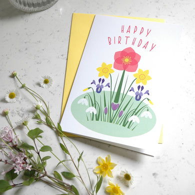 Birthday card with floral design and 'Happy Birthday' text on a light surface with flowers.
