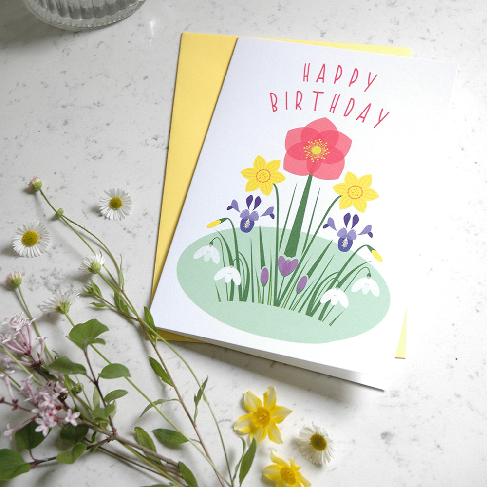 Birthday card with floral design and 'Happy Birthday' text on a light surface with flowers.