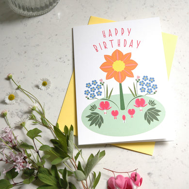 Birthday card with floral design and 'Happy Birthday' text on a light surface with flowers.