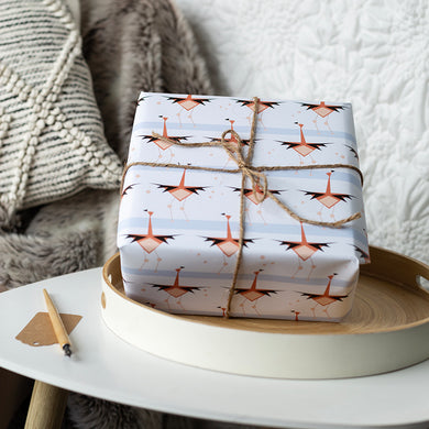 Gift wrapped in flamingo-patterned paper on a white surface with a textured background