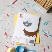 Load image into Gallery viewer, The back of a greetings card labeled 'Big Dog Hugs' by Nose to toes, placed on top of a yellow envelope on a light surface scattered with confetti. A box of wooden matches are partially visible in the upper right.