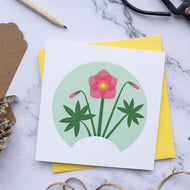 Small card with illustration of a Hellebore full flower with two buds and two leaves. The card is on top of a yellow envelope which is on top of a marble surface.