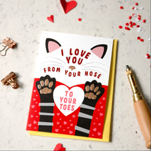 Load image into Gallery viewer, A novelty greeting card with a cat-face illustration and the text 'I LOVE YOU FROM YOUR NOSE TO YOUR TOES,' shown on a light speckled surface with red hearts, paper clips, and a paper drill around it.