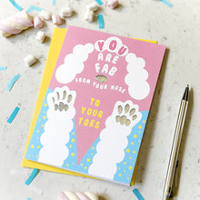 Load image into Gallery viewer, A pink and blue greeting card with white paw prints and the text 'YOU ARE FAB FROM YOUR NOSE TO YOUR TOES', placed on a light marble surface with a yellow envelope, marshmallows, confetti, and a pen around it.