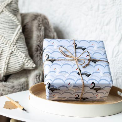 Gift wrapped in blue paper with black swan design on a white surface.