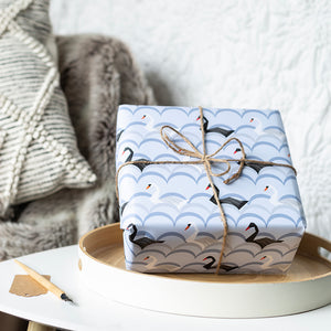 Gift wrapped in blue paper with black swan design on a white surface.