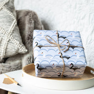 Gift wrapped in blue paper with black swan design on a white surface.